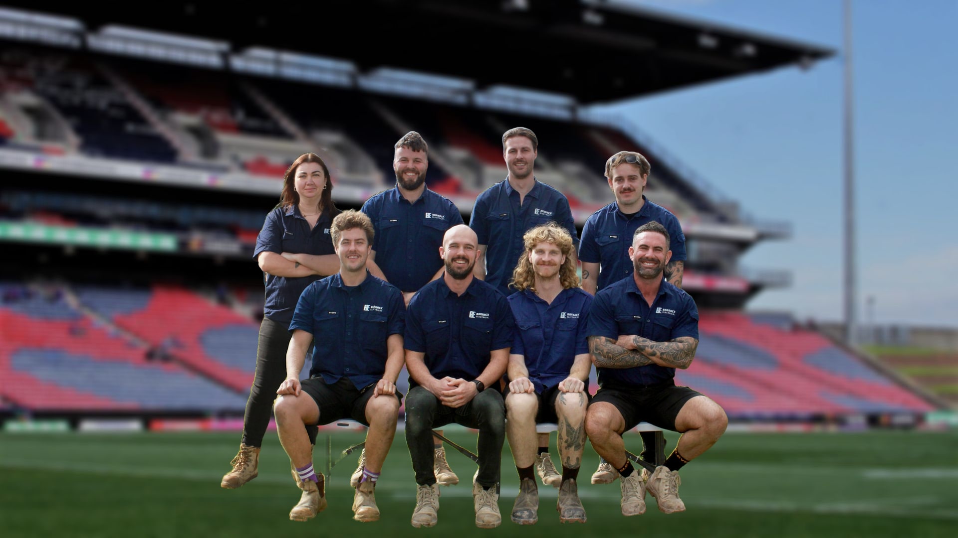 The Barrack Electrical team of eight in uniform, four standing and four seated, on the field in front of the grandstand at the Newcastle stadium