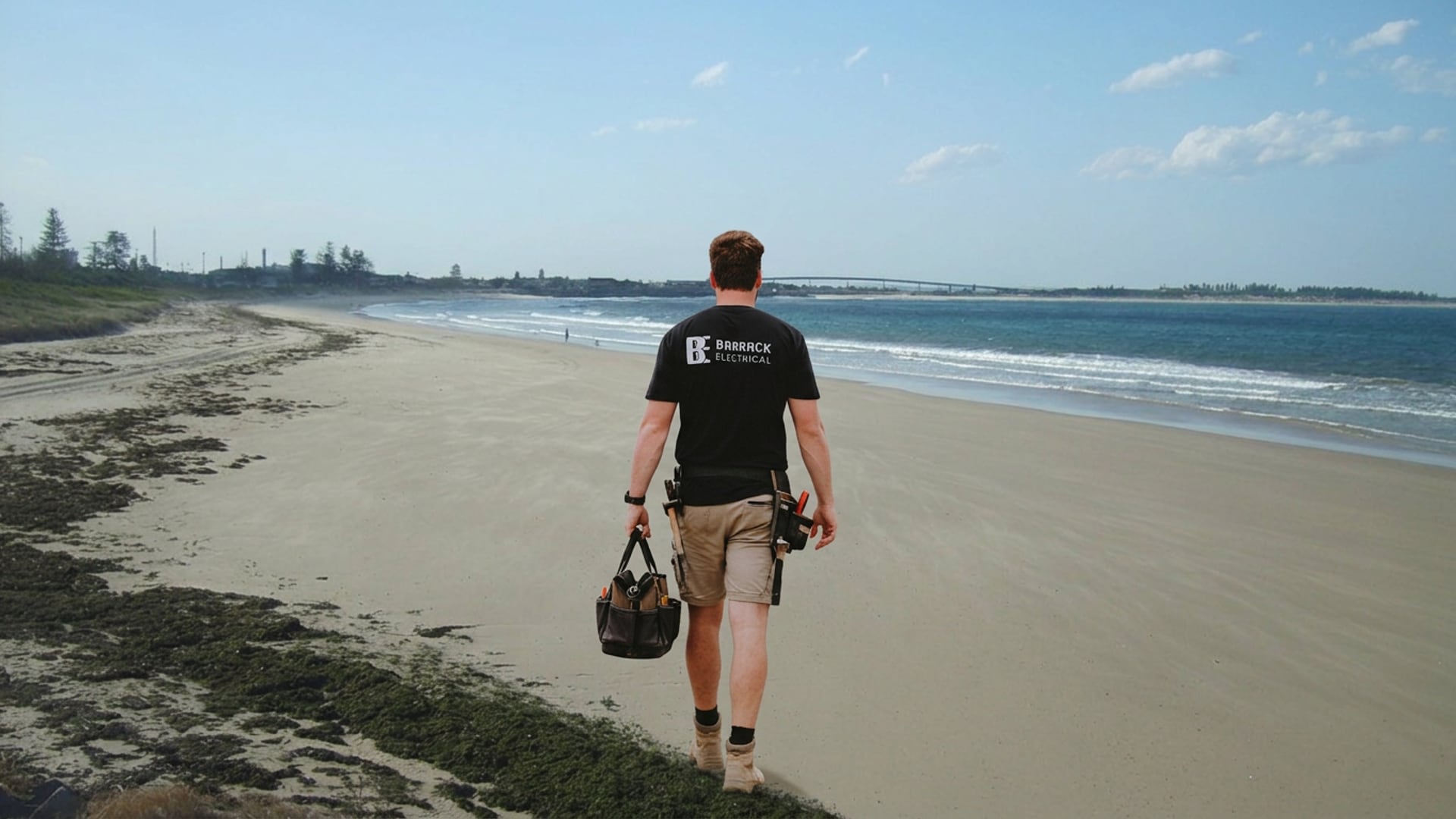 A Barrack Electrical electrician walking the sand at Stockton Beach with a tool bag