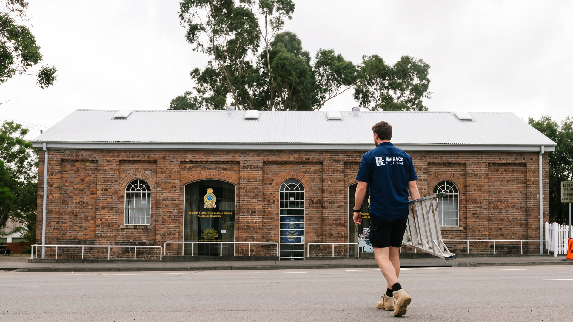 A Barrack Electrical electrician carrying a step ladder past the heritage railway goods shed at Wallsend