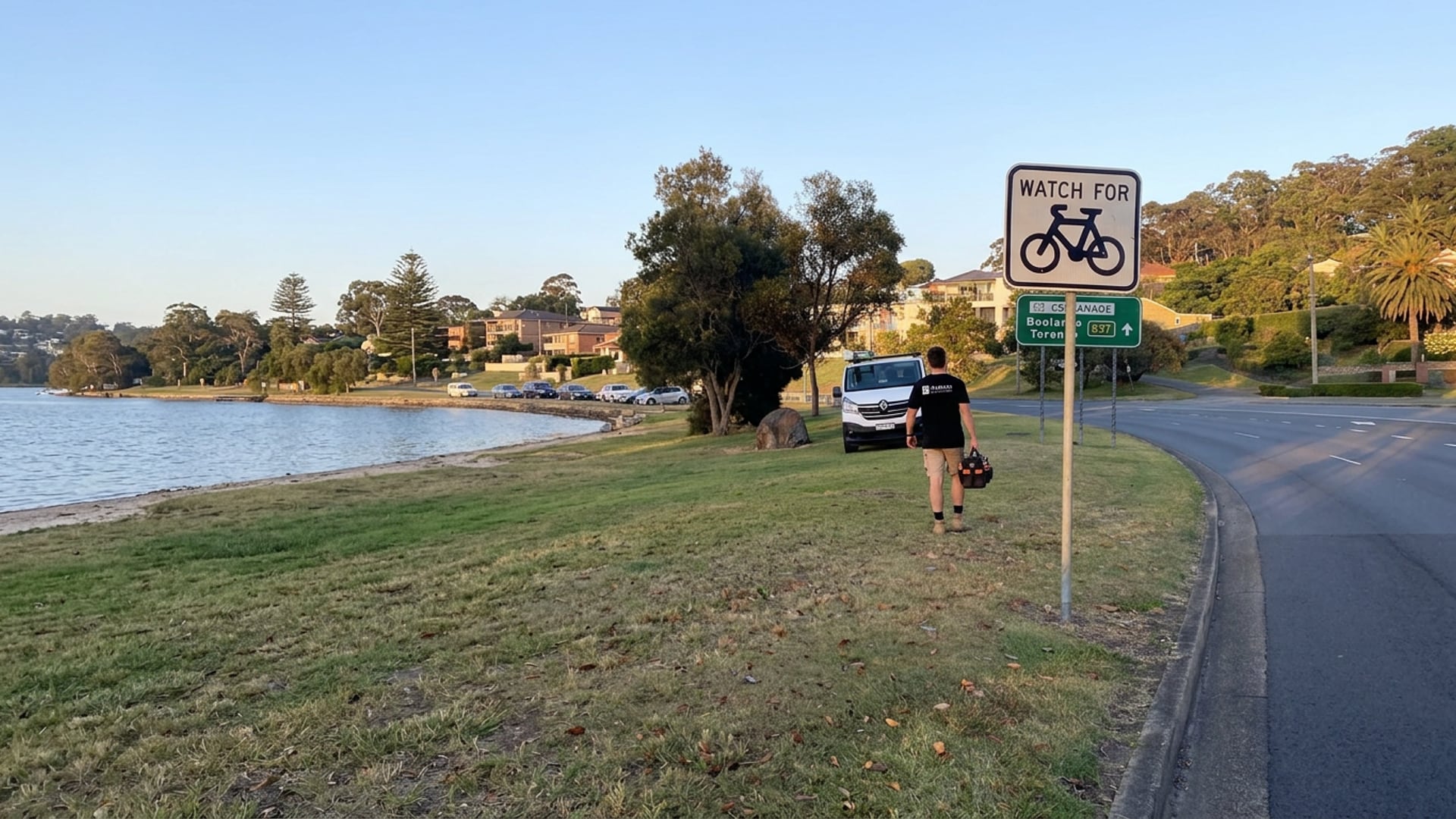 A Barrack Electrical electrician on the foreshore grass at Warners Bay, the lake behind