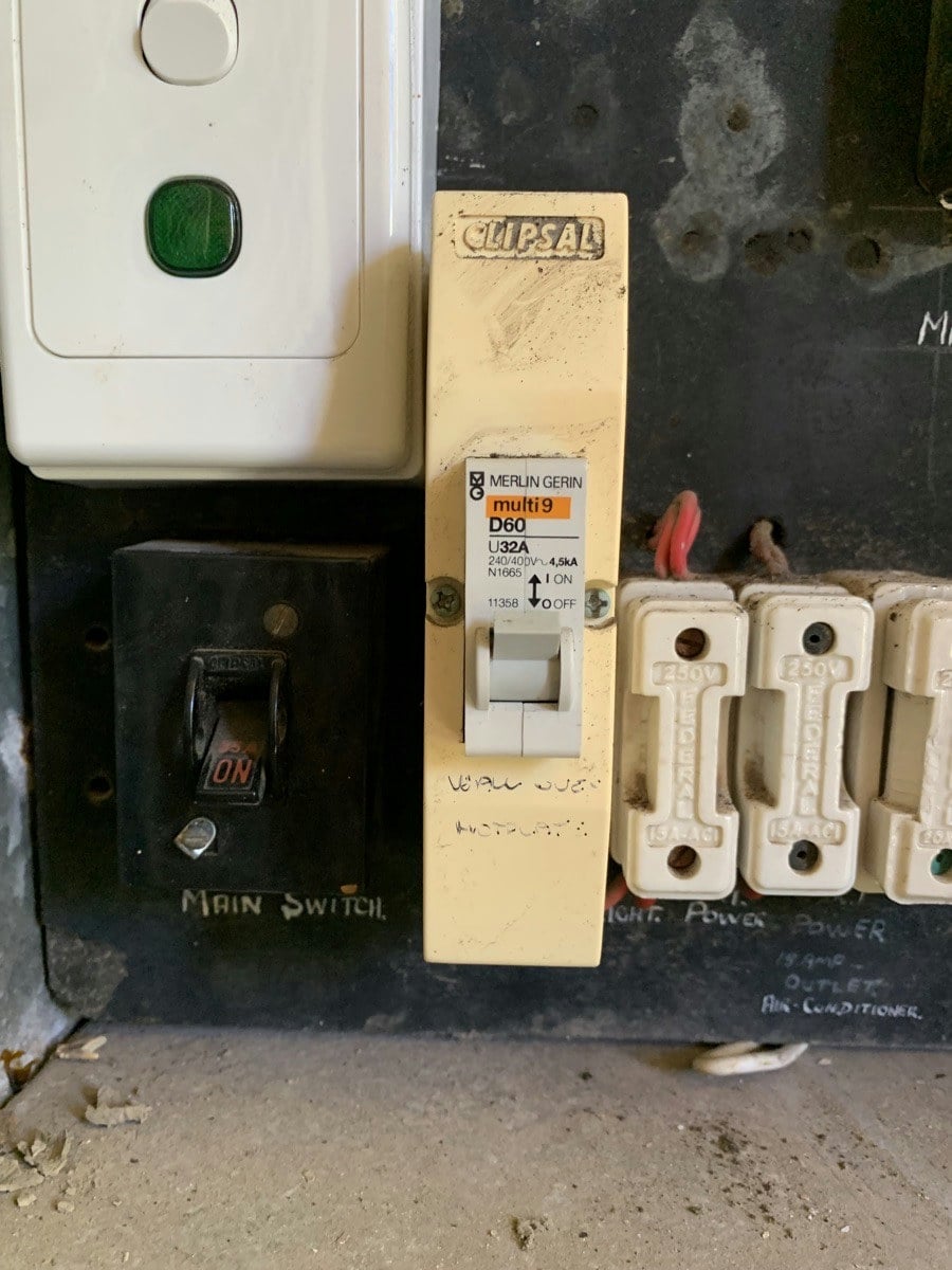 A mixed switchboard: a bakelite main switch, ceramic fuses and a later breaker on the same panel
