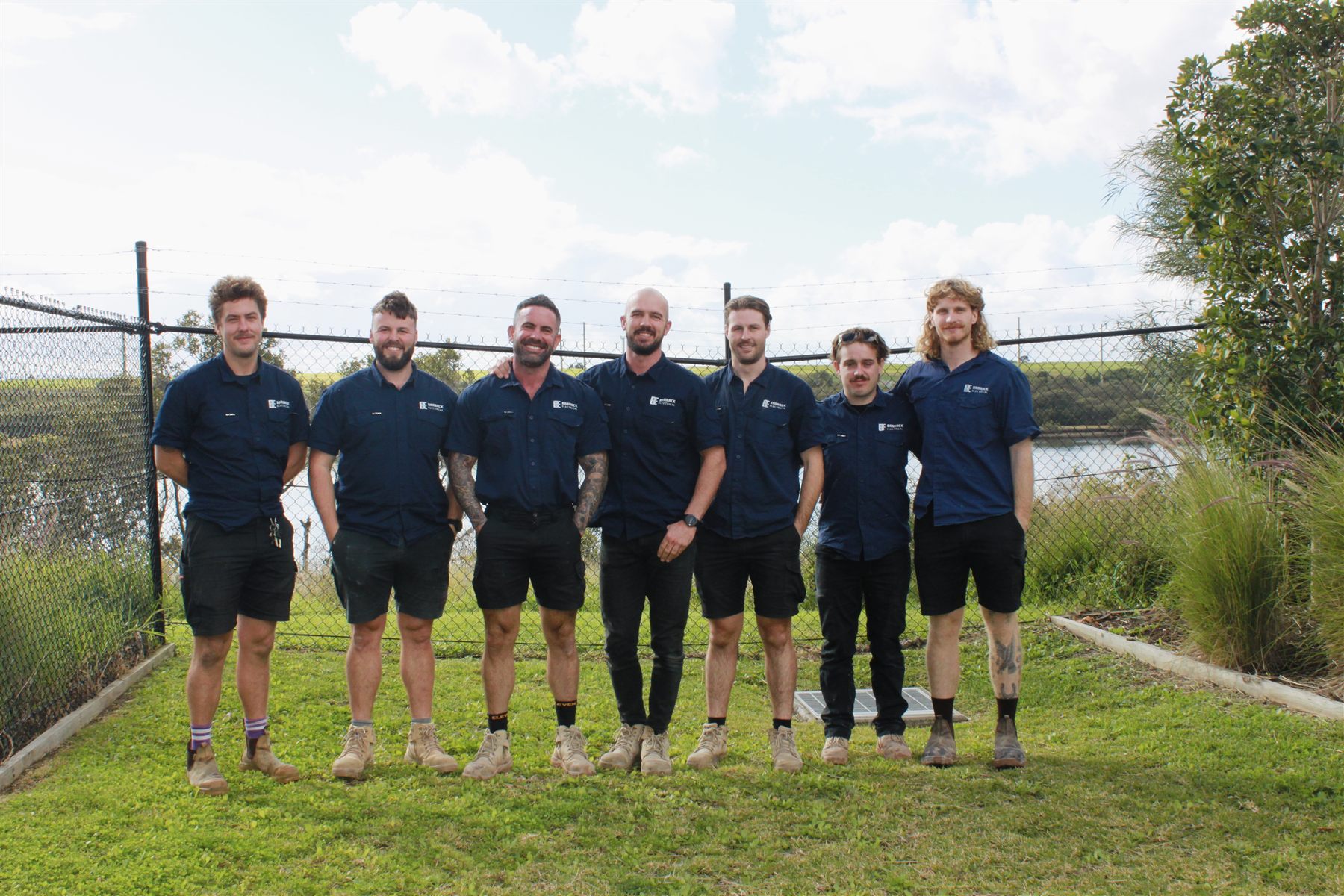 The Barrack Electrical team of seven in uniform, standing together by the water