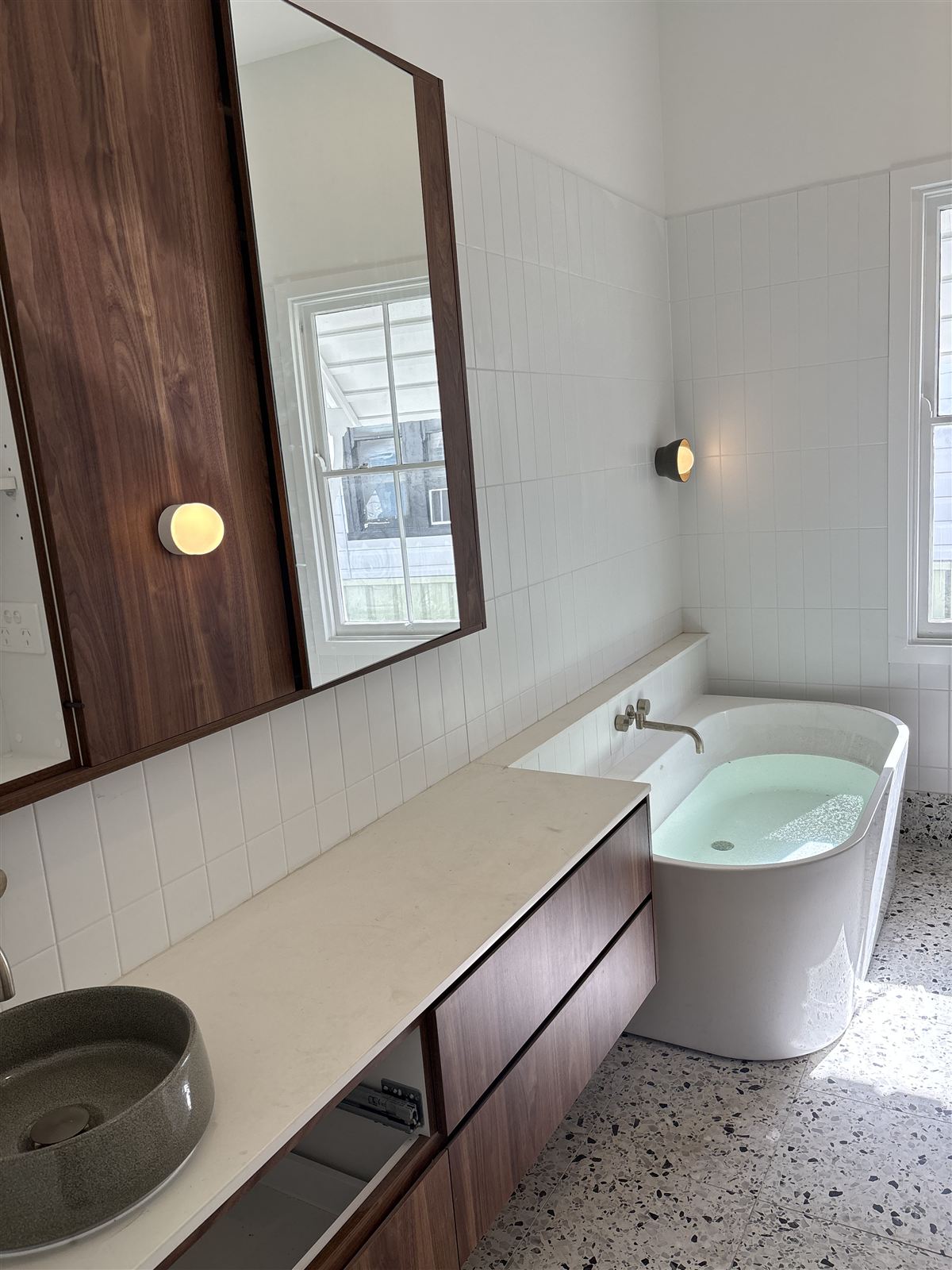 Renovated bathroom with wall lights, a timber mirror cabinet and freestanding bath