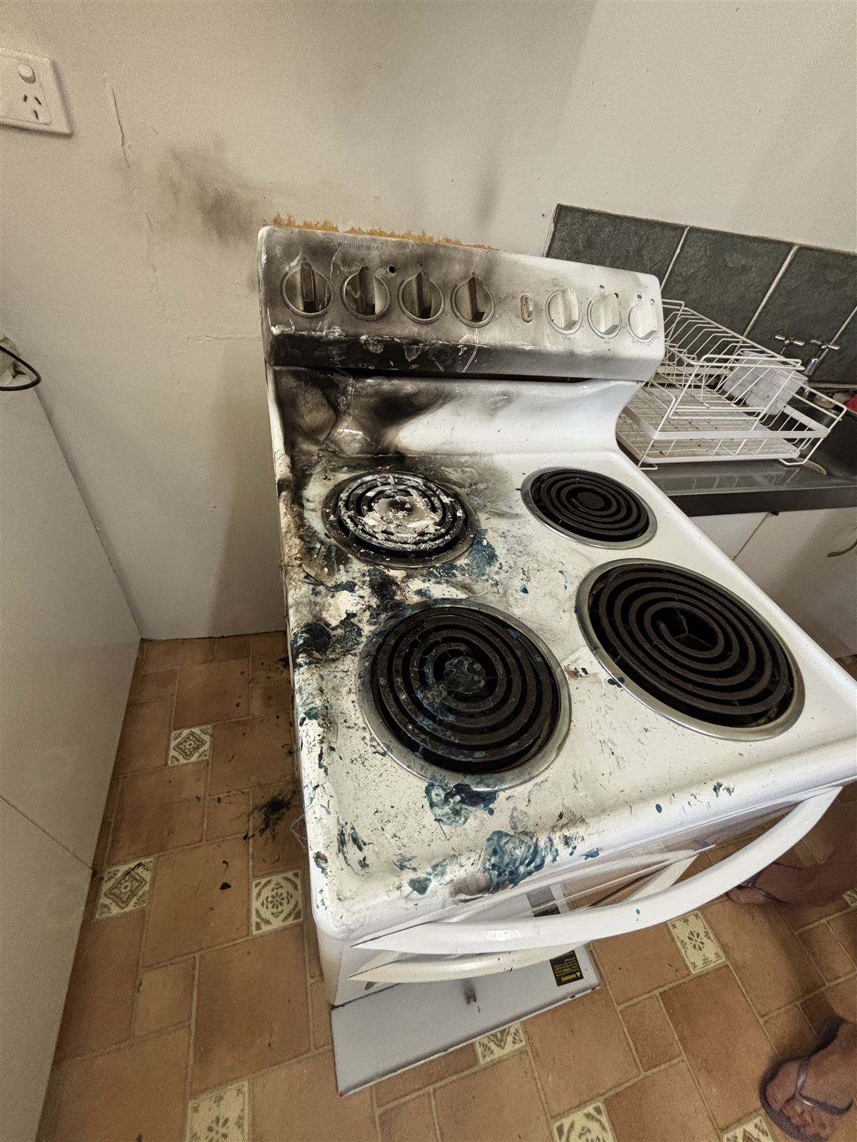 Electric stove badly burnt and blackened, with scorching on the wall behind it