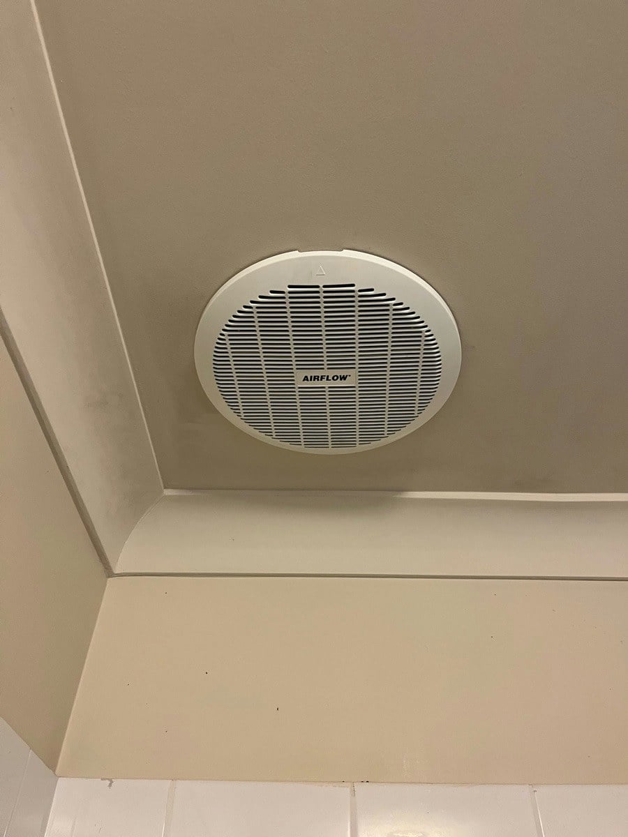 A round exhaust fan set into a sloped ceiling above a tiled wall