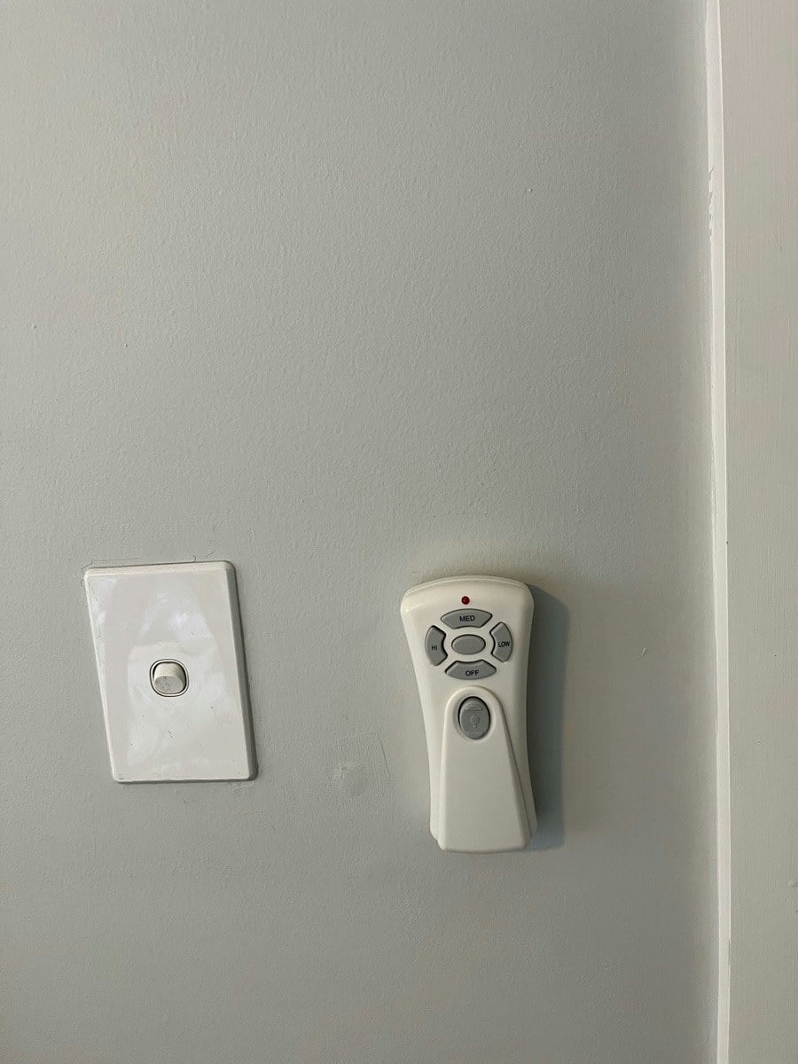 A ceiling fan remote in its wall cradle beside the light switch