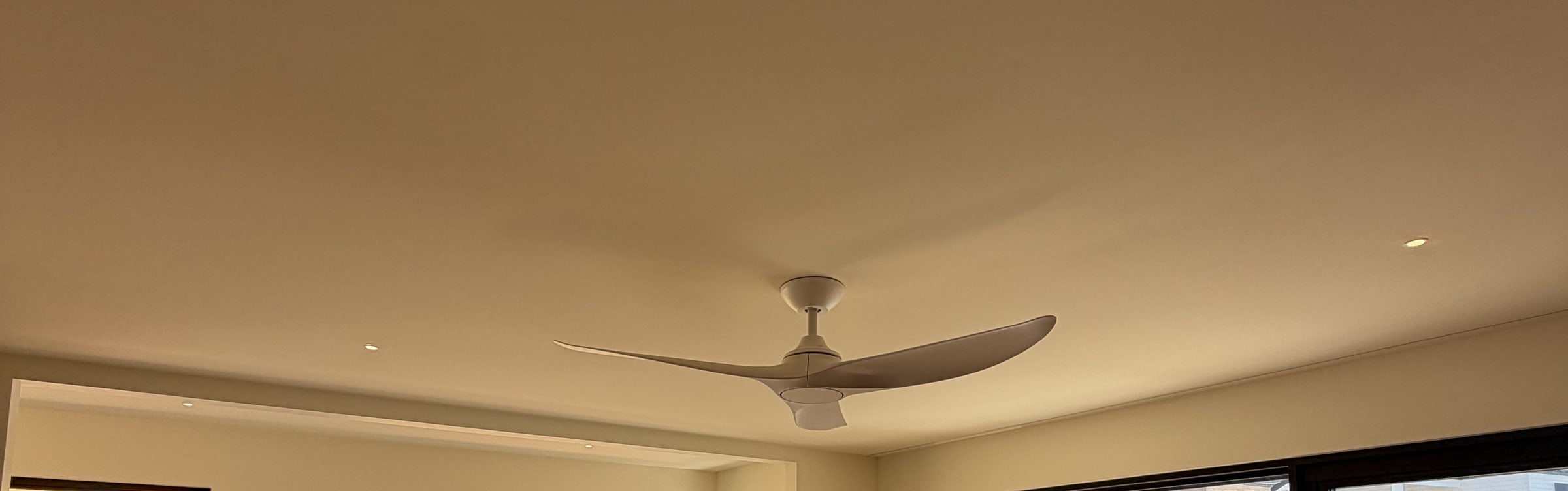A three blade DC ceiling fan with an integrated light fitted to a bedroom ceiling, downlights around it