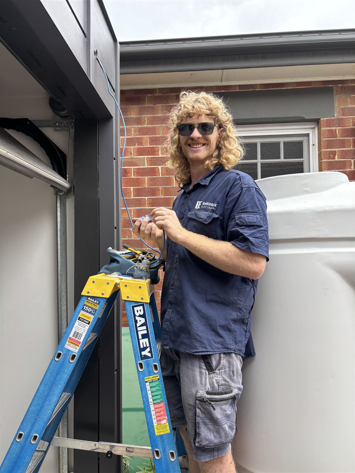 Electrician on a step ladder running new cable outside a brick home