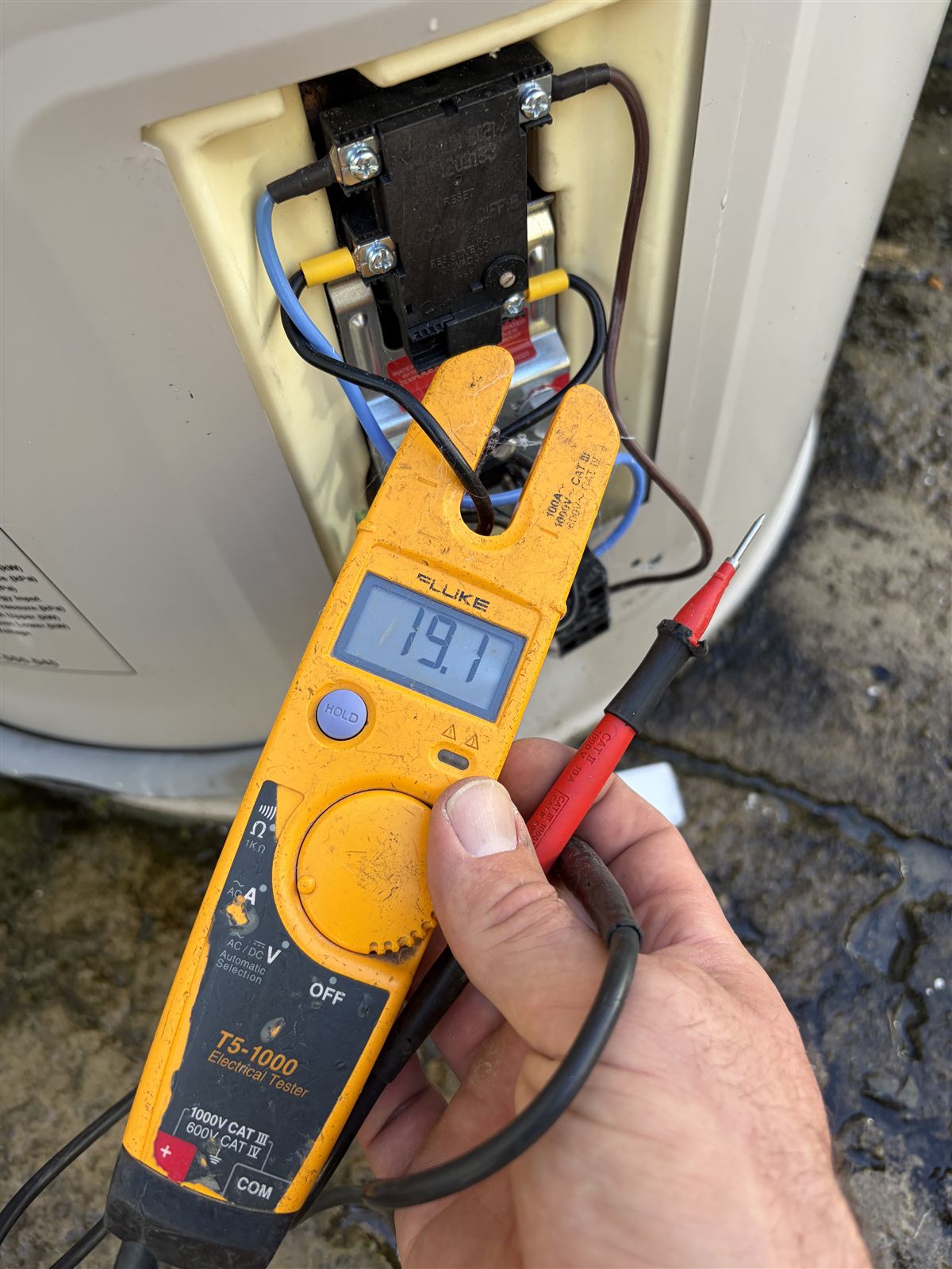 Electrician testing a hot water system's electrical connection with a clamp tester