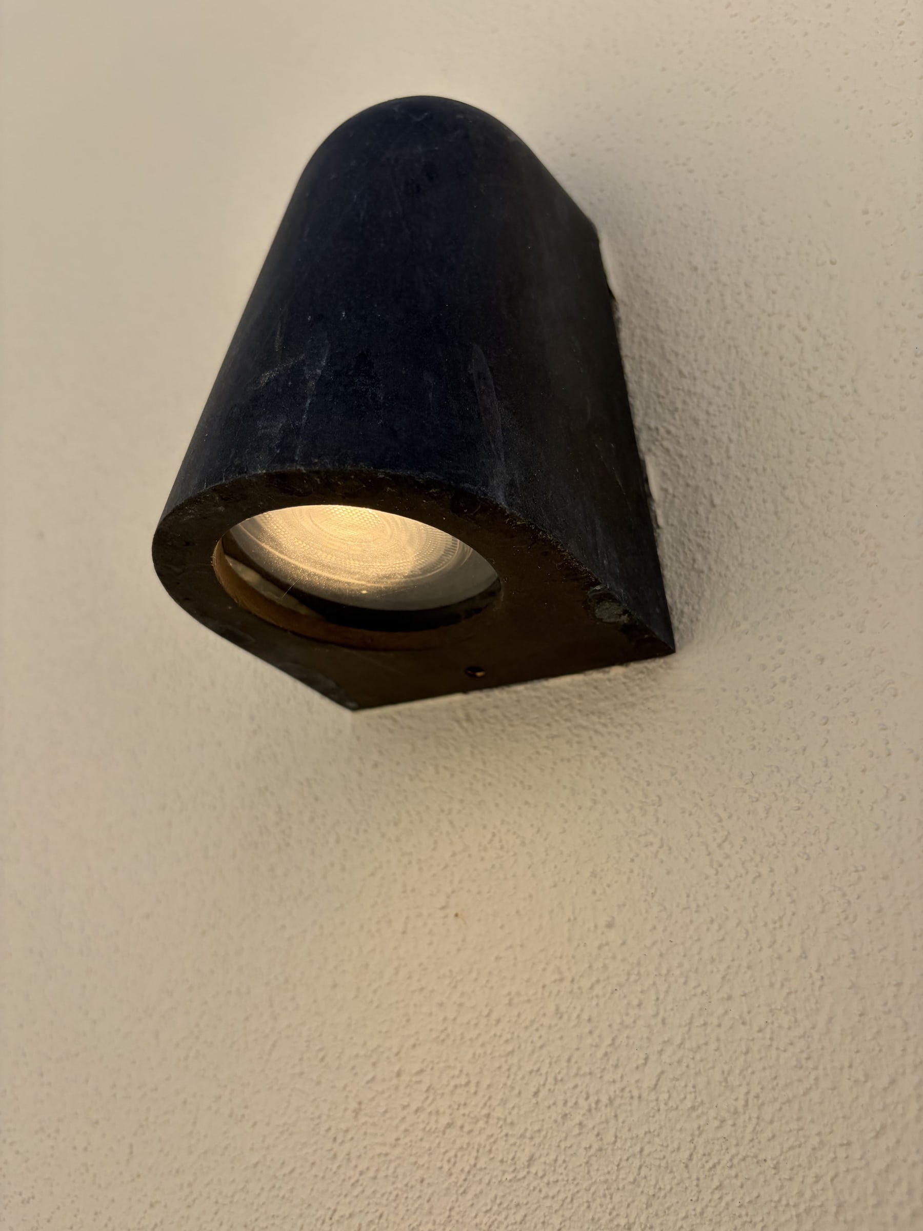 A black exterior wall light mounted on a rendered wall, lit
