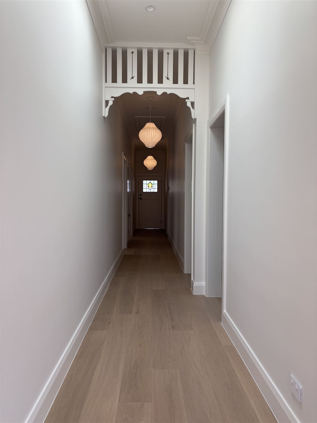 Pendant lights down the hallway of a period home, under a timber fretwork arch