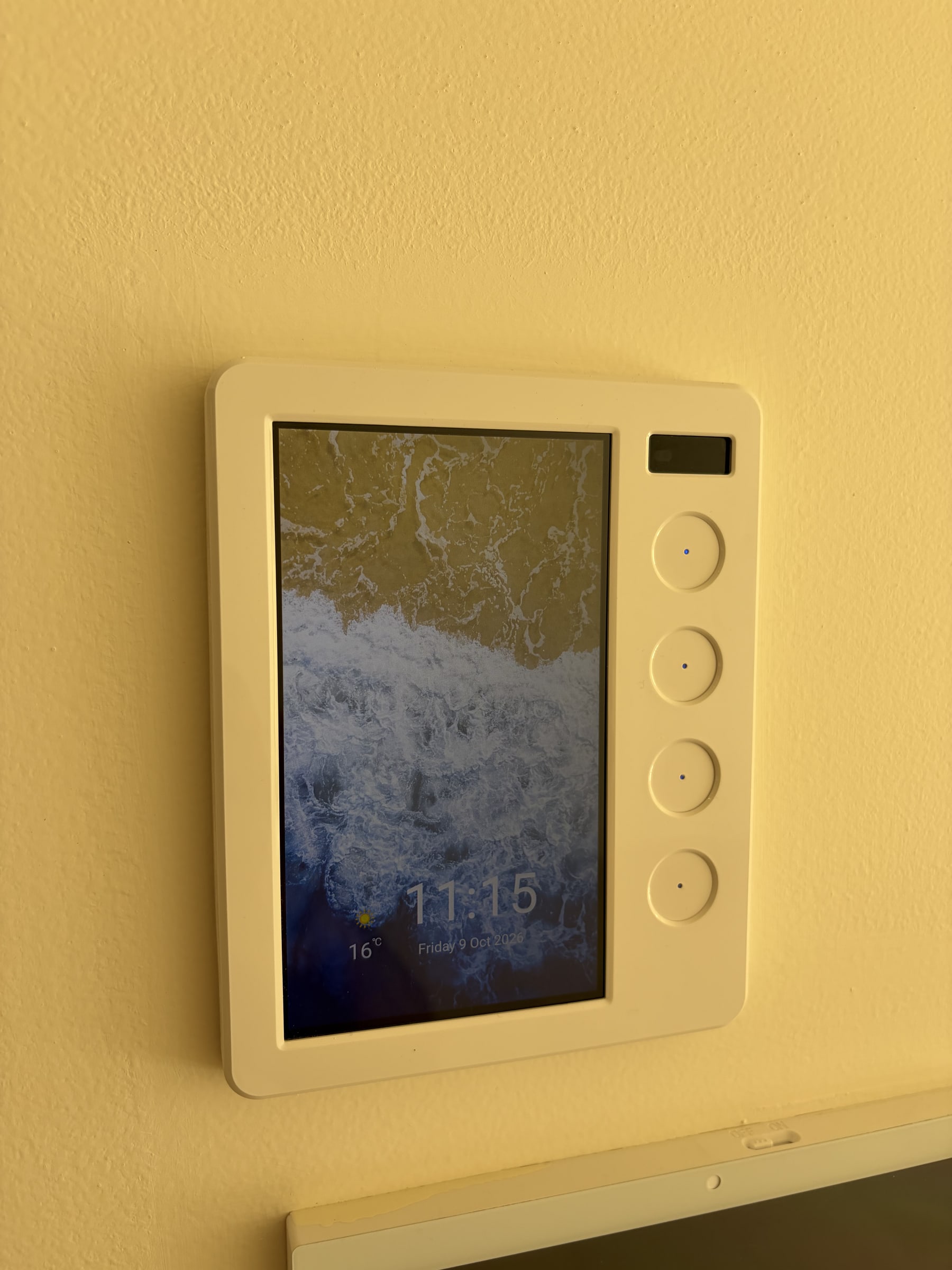 A wall-mounted home automation touch panel with four dimmer buttons beside the screen