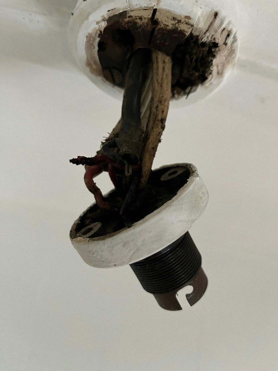 Cracked and crumbling black rubber insulated cable running into an old porcelain ceiling rose