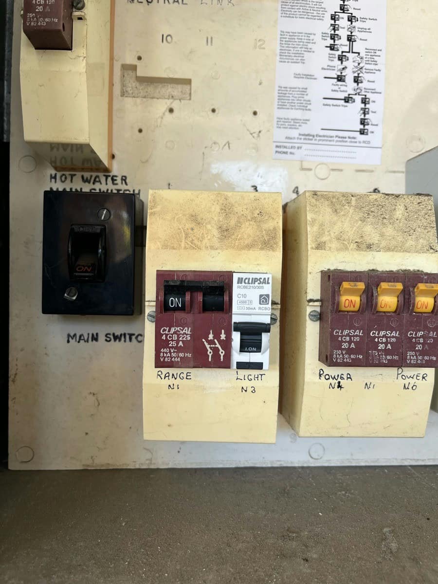 An old board with a bakelite main switch and two banks of ceramic fuse carriers hand-labelled Range, Light and Power