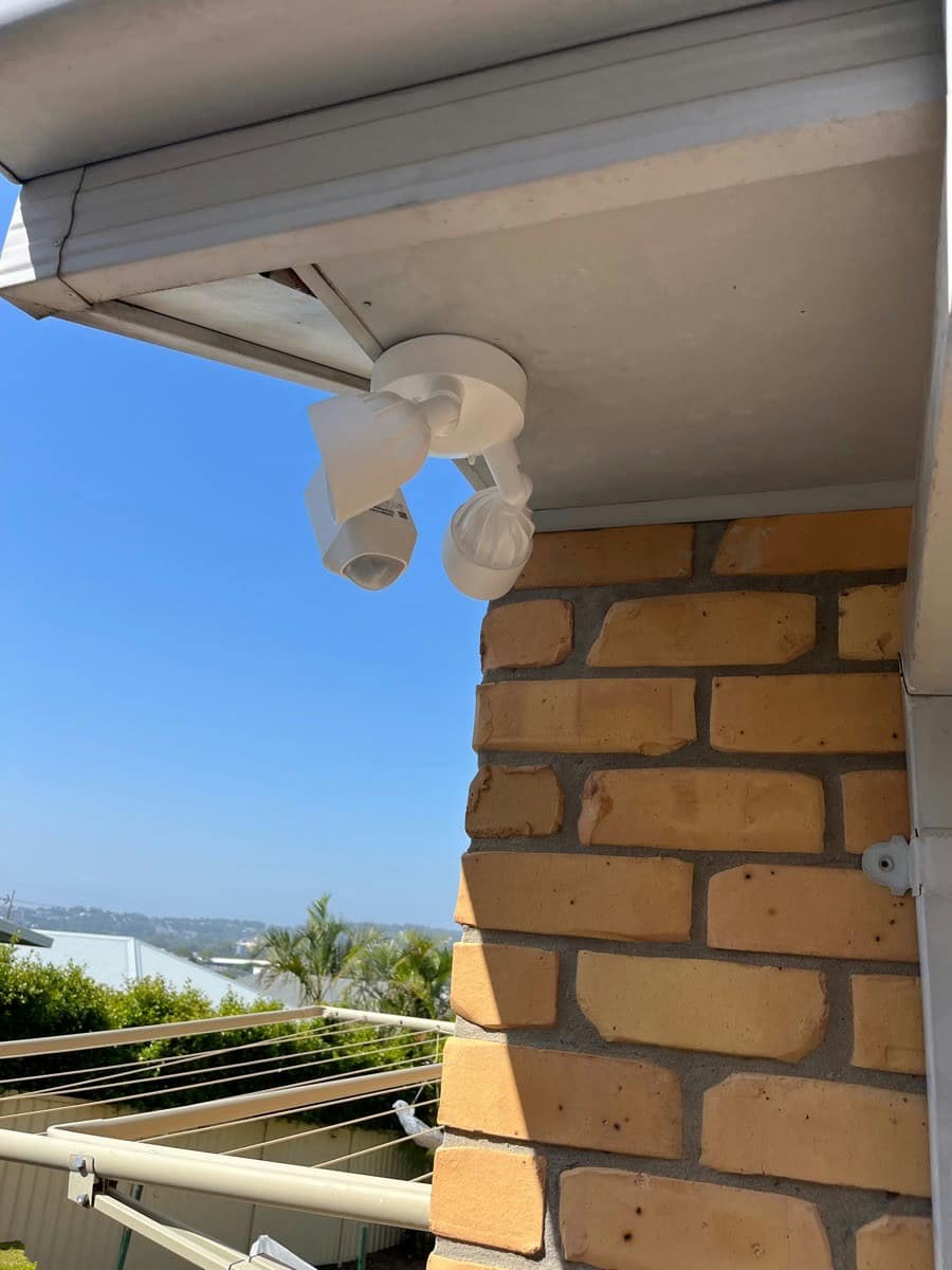 A CCTV camera and sensor light fitted together under the eaves of a home