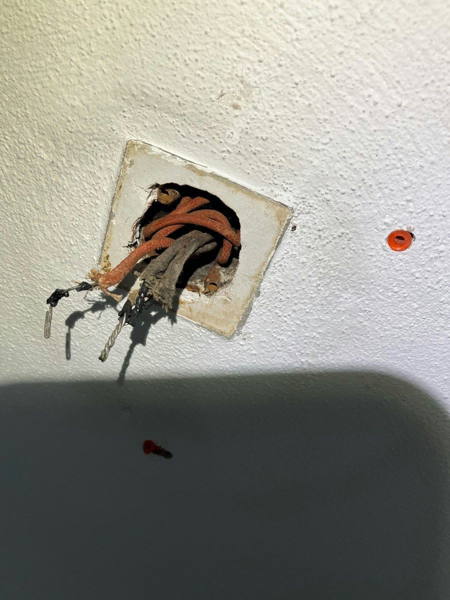 Cable hanging from a ceiling opening with the sheath burnt away and soot staining the plaster