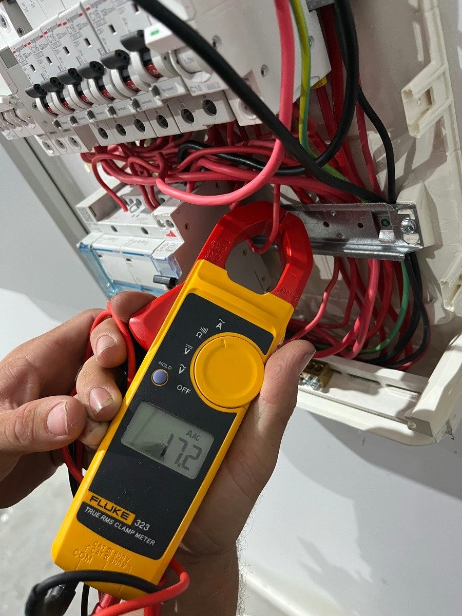 A clamp meter placed around a conductor at an open switchboard