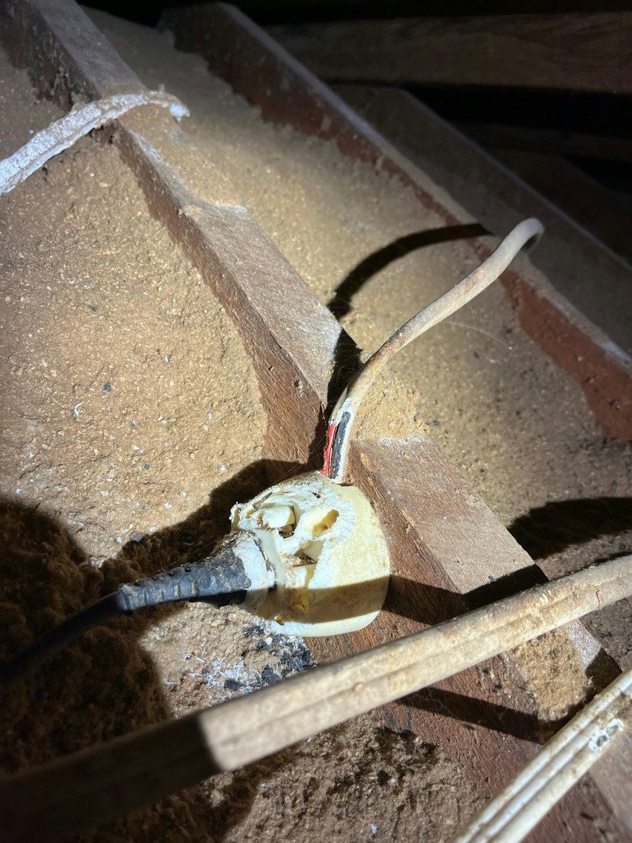 A cracked porcelain fitting and old cable in a dusty roof space
