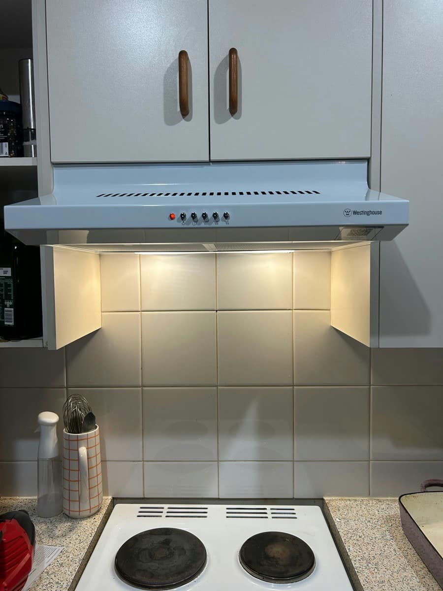 A range hood with its light on above a coil cooktop