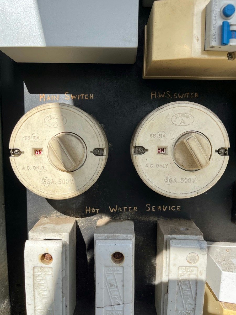 Two large round porcelain main switches on an old black switchboard panel above a row of ceramic fuses