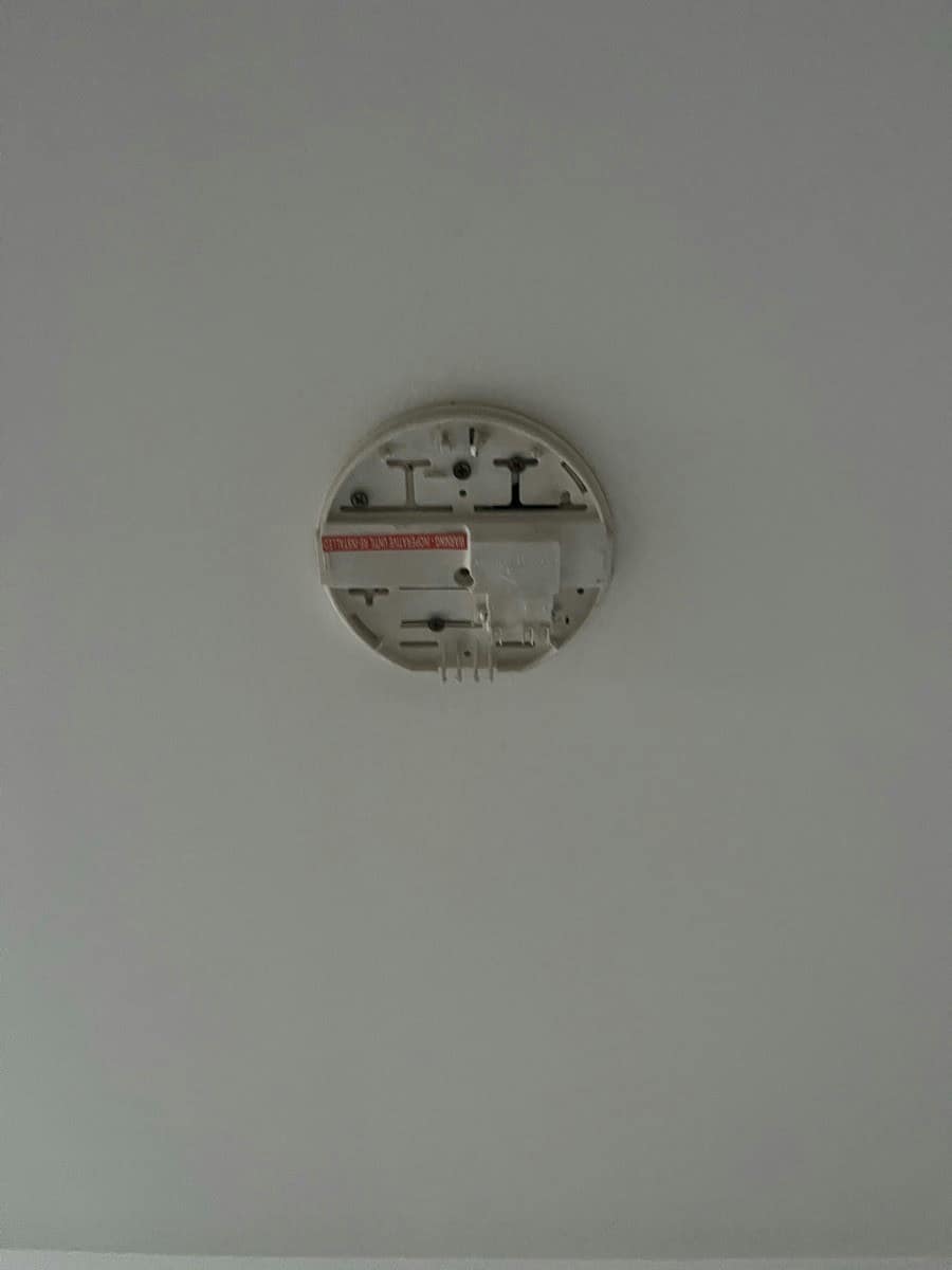 An old smoke alarm base opened at the ceiling with the cover off and the terminals exposed