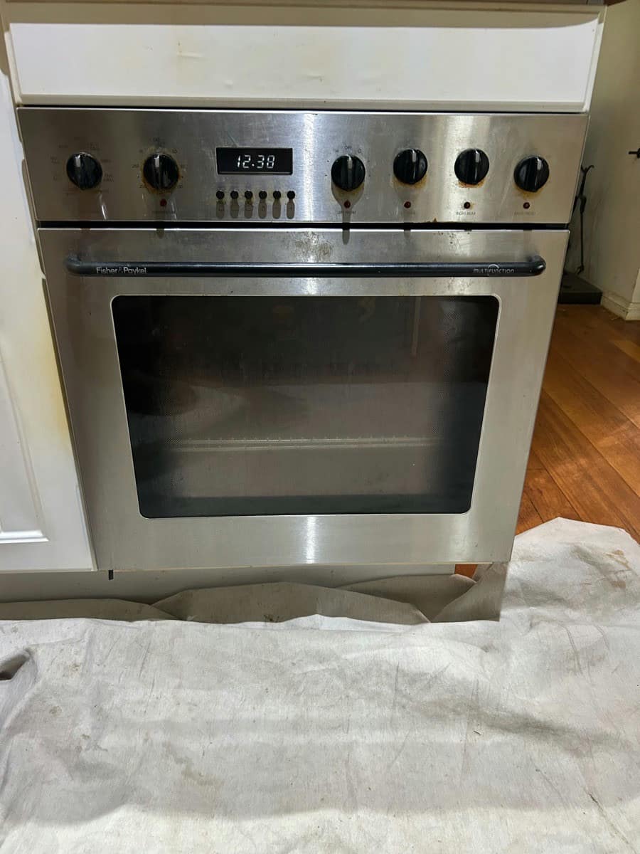 A stainless wall oven pulled out of its cabinet onto a drop sheet