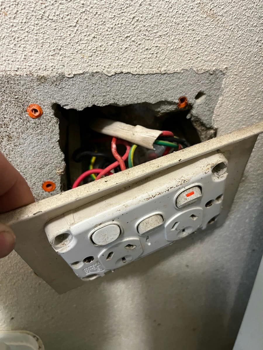 A double power point drawn out of the wall on its cable, the old conductors visible in the cavity behind