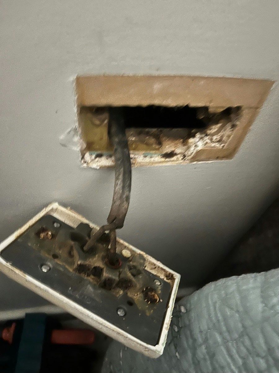 A power point hanging from a wall on charred cable with the cavity behind it scorched black