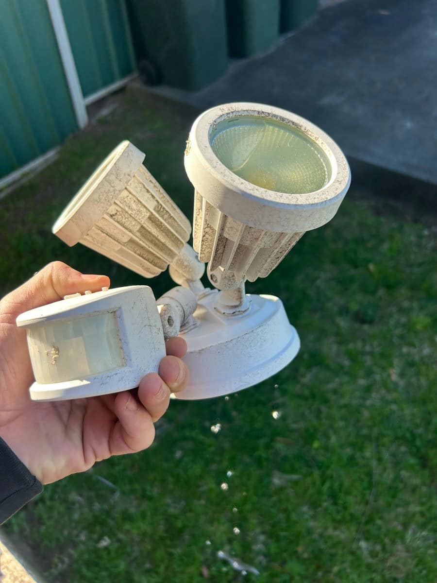 A removed twin spot sensor light held up, the housing dirty and the lens clouded