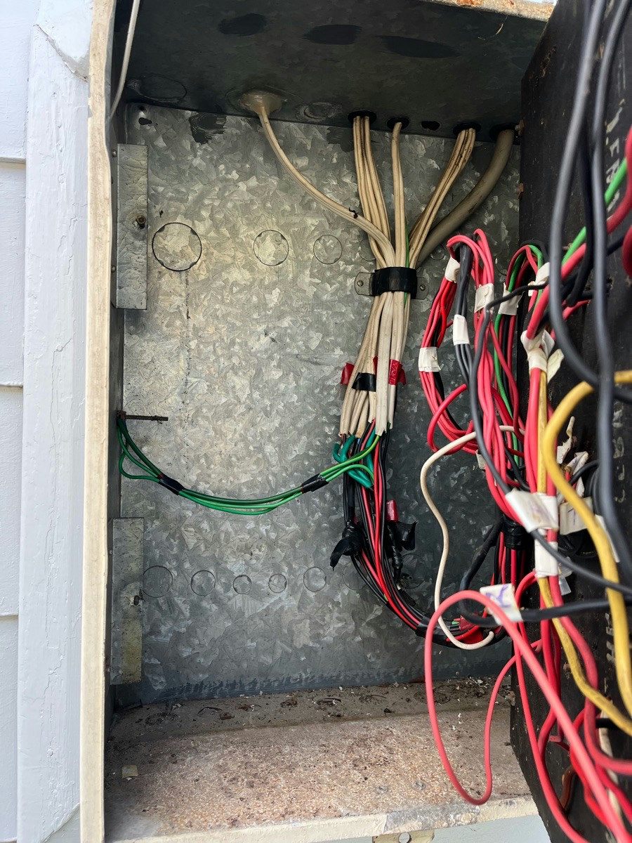 A bundle of cotton-braided cables inside an old switchboard enclosure beside newer conductors