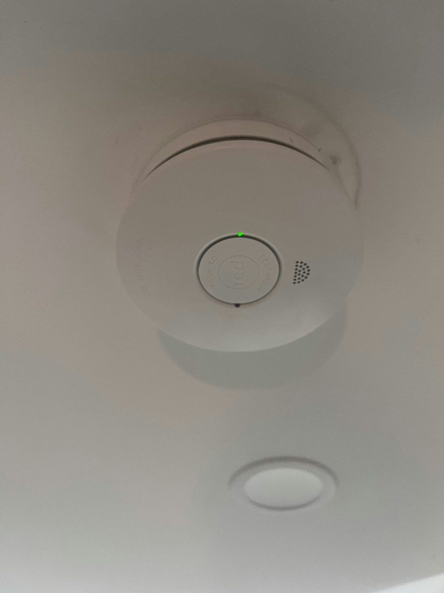 A new smoke alarm on a ceiling with its green power indicator lit and the test button visible