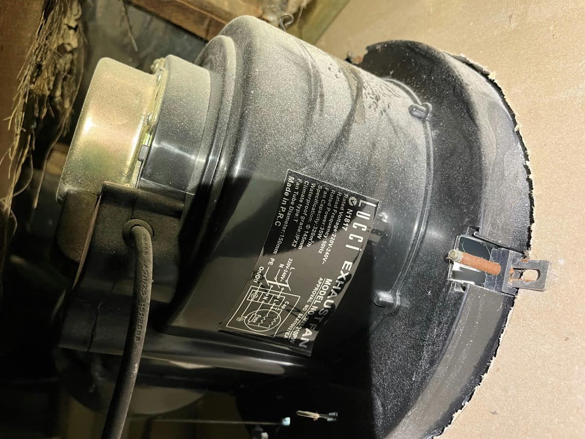 An exhaust fan assembly pulled from a ceiling, the housing and motor furred with dust
