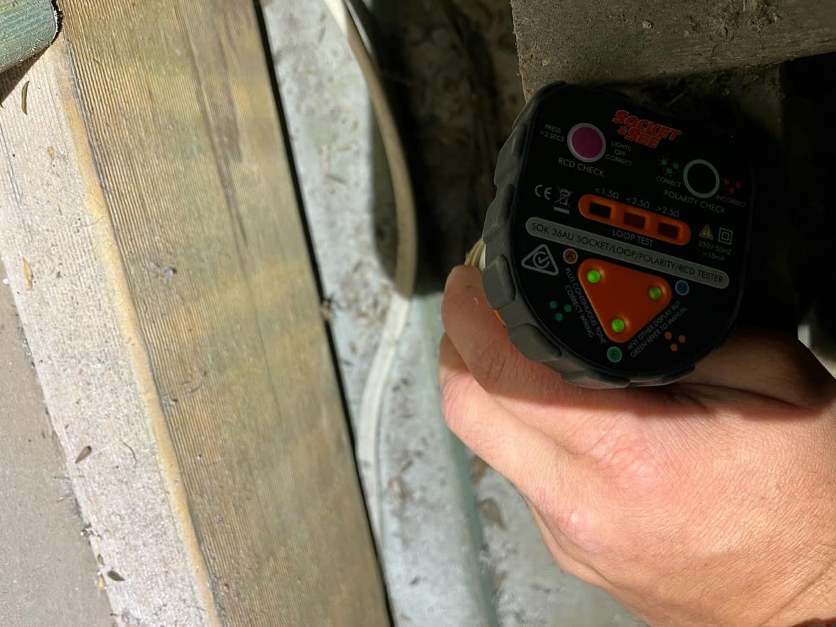 A socket tester held against weathered timber in an underfloor space