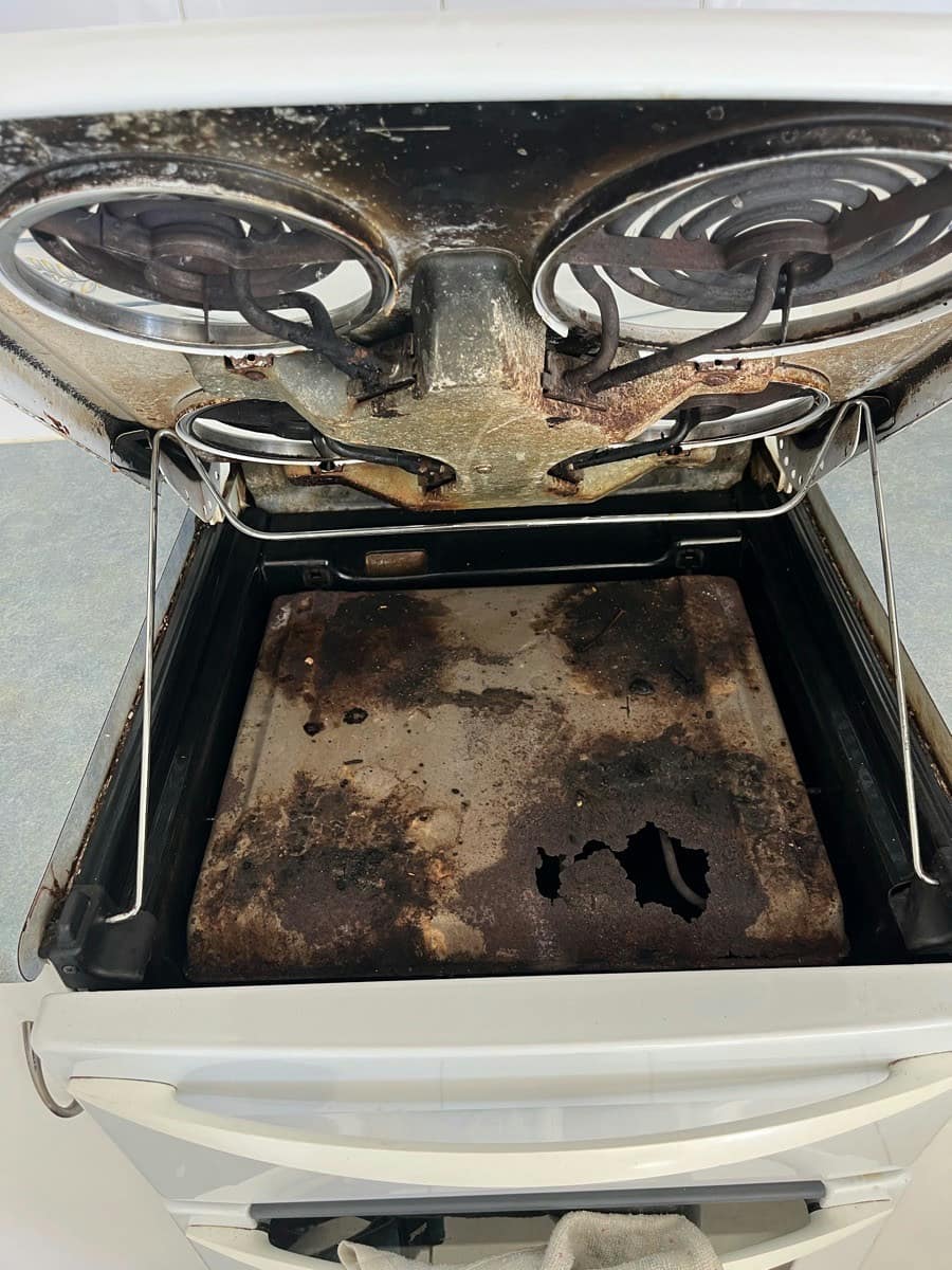 A worn stove with the cooktop raised and the oven cavity blackened