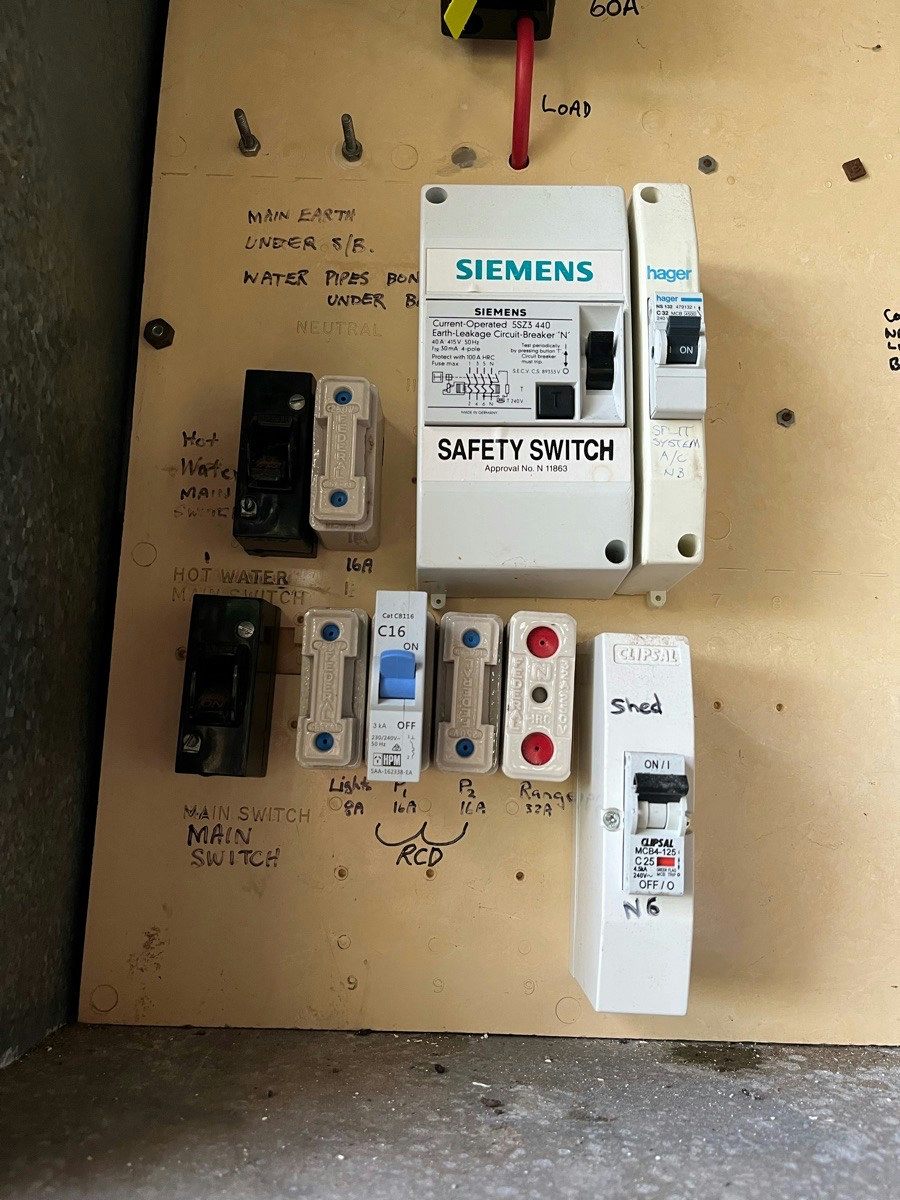 An older board with one safety switch fitted among old switches and fuses, the other circuits unprotected