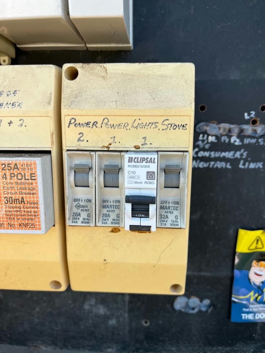 An old fuse panel with the circuits hand-lettered Power, Power, Lights and Stove beside a newer earth leakage breaker