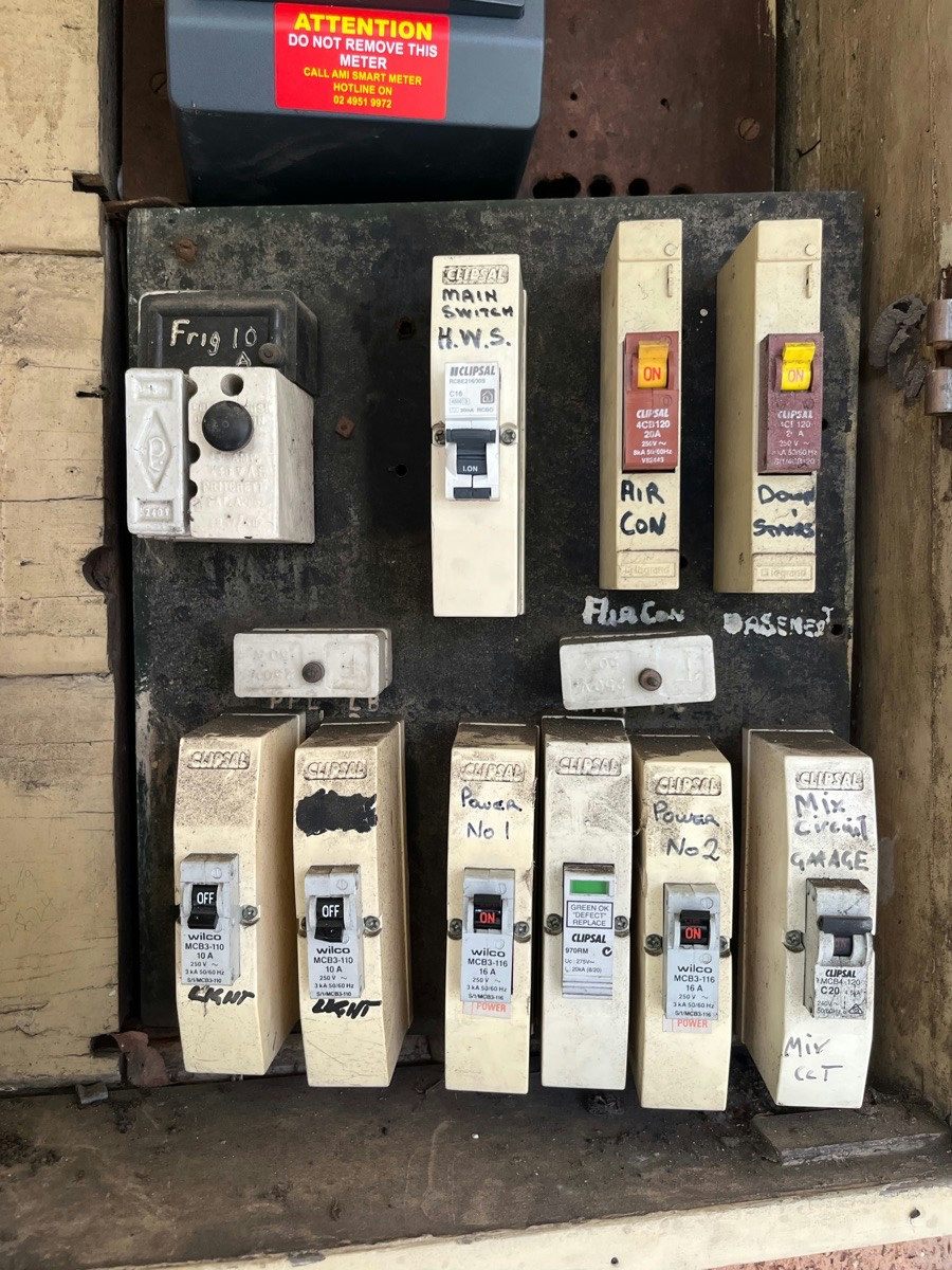 An open meter box with a row of old ceramic fuse carriers, each hand-labelled by circuit