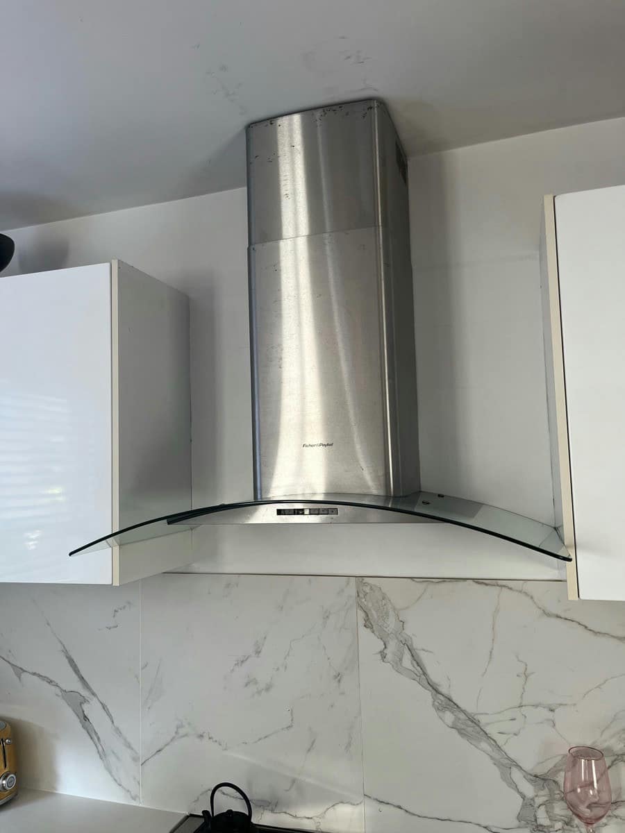 A stainless canopy range hood between overhead cupboards