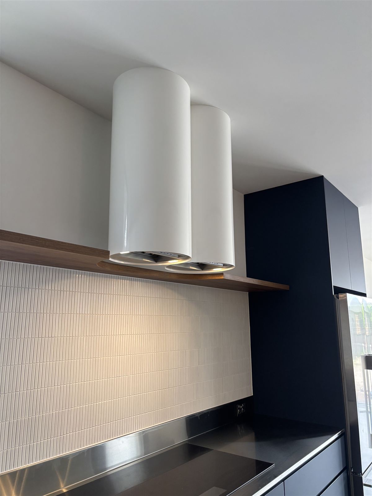 Twin range hoods installed above a cooktop in a finished kitchen