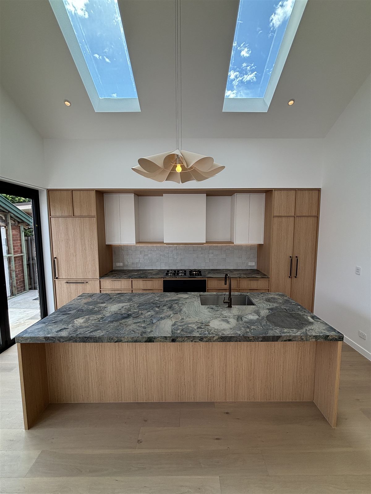 Sculptural pendant light over a stone kitchen island, with LED downlights and skylights