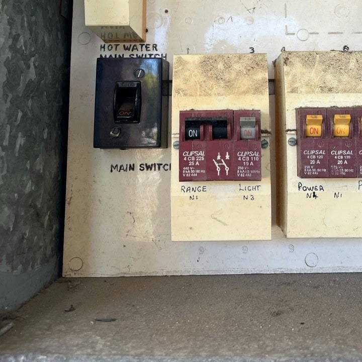 An old bakelite main switch beside fuse carriers labelled range, light and power