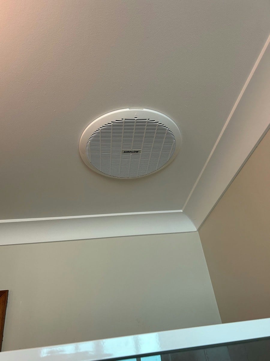 A large oval exhaust grille set into a white bathroom ceiling