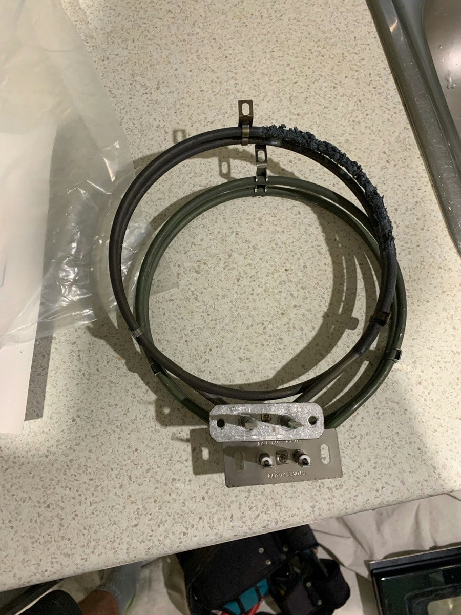 A burnt-out fan oven element on the benchtop beside its replacement