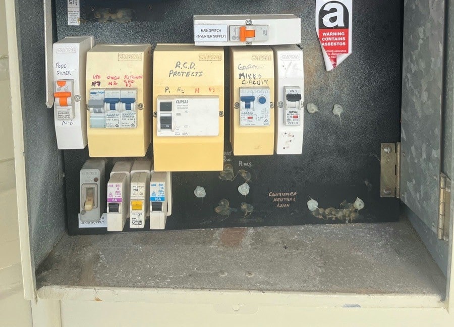 An older switchboard carrying an asbestos warning label, with safety switches fitted to some circuits