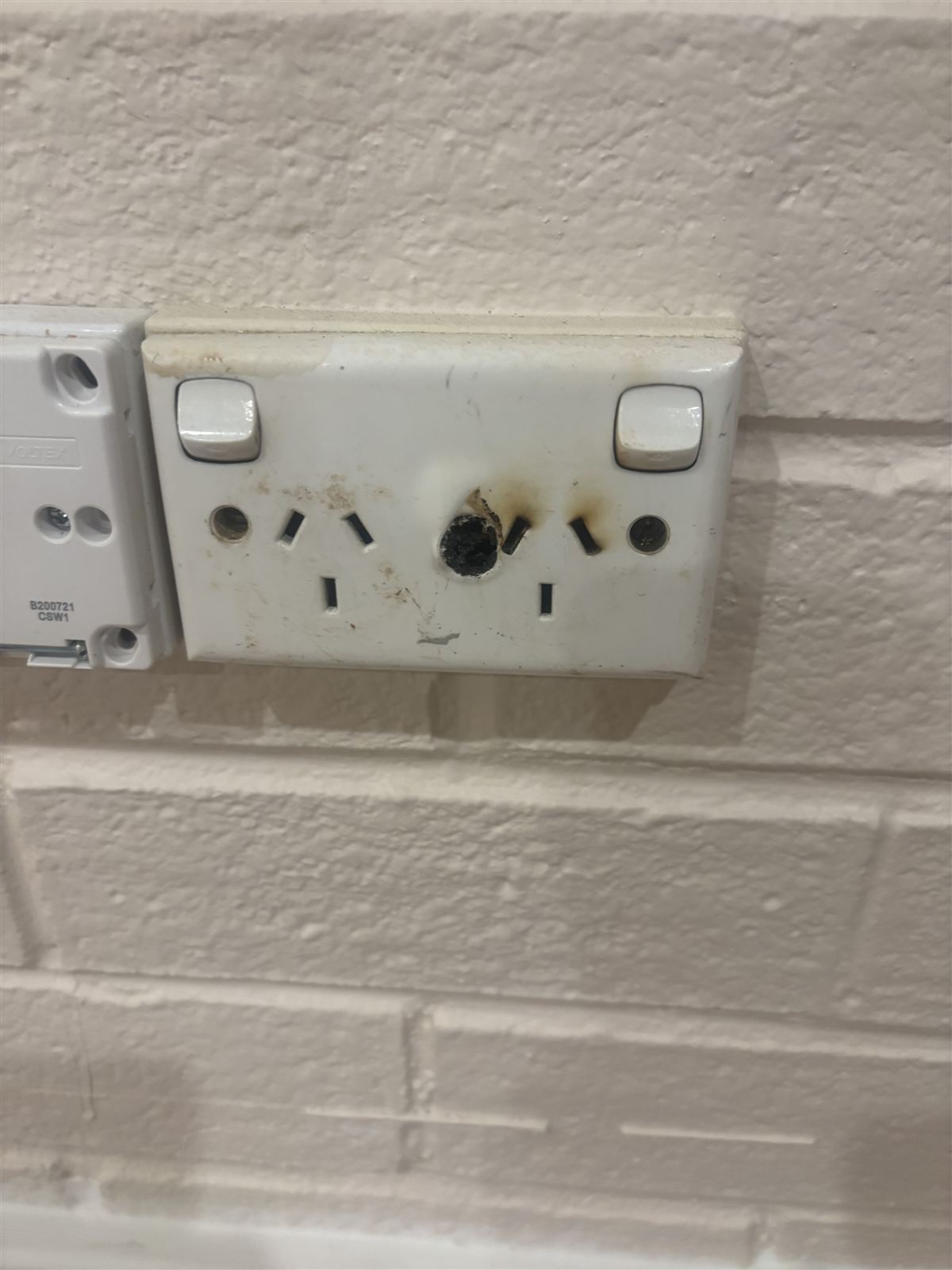 Scorched double power point on a painted brick wall, no longer safe to use