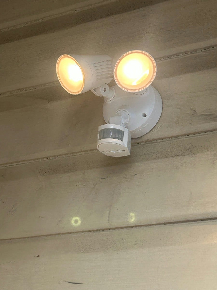 A twin-spot sensor light on a house wall, both lamps lit and the sensor angled below