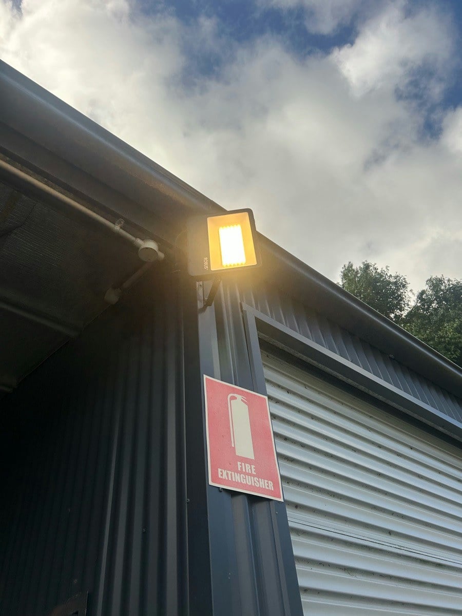 An LED flood light lit on the corner post of a shed beside a roller door
