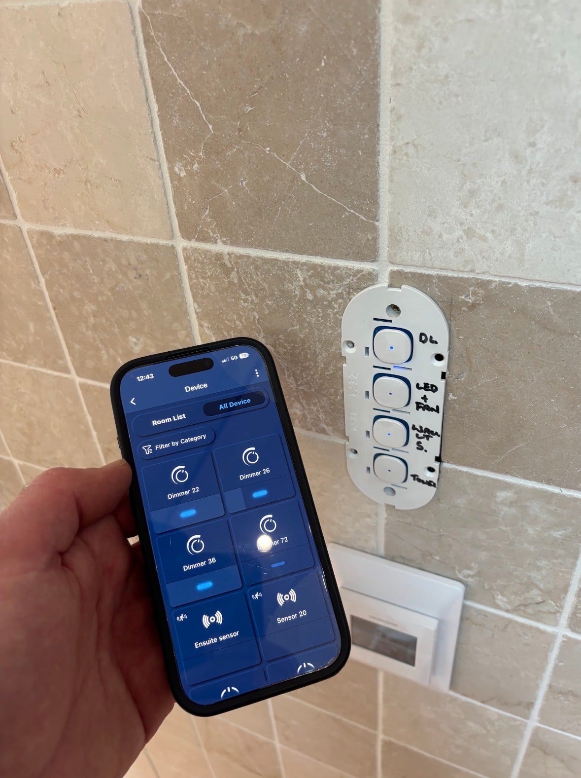 The smart home app open on a phone beside the smart switch on the wall