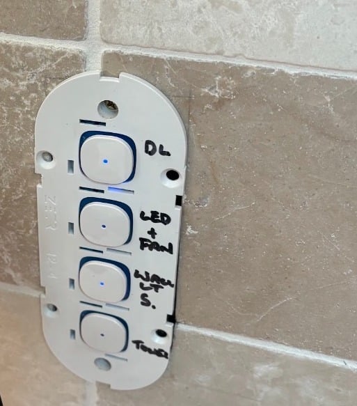 A four-button smart switch on a tiled wall with its buttons lit