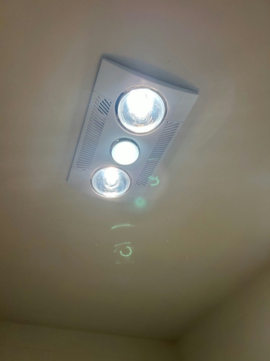 A three-in-one unit lit in a bathroom ceiling, the heat lamps and centre light on